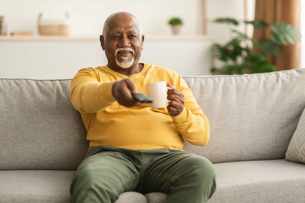 older man watching tv with coffee in his hand