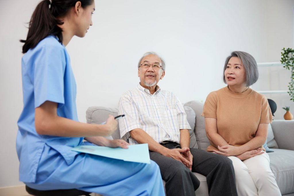 Elderly Asian couple discussing home health services with a young female caregiver.