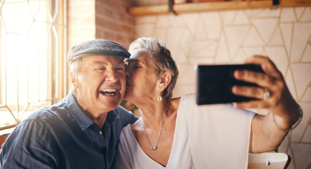 senior selfie couple, woman kissing man on the cheek and both smiling