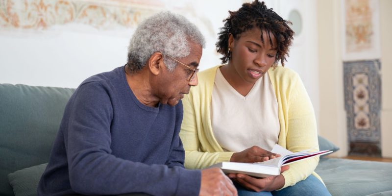 elderly man and younger woman sitting on couch reading together