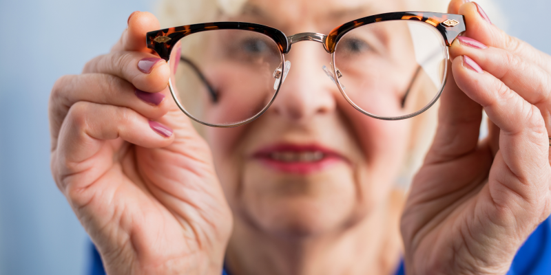 senior woman holding up a pair of eye glasses