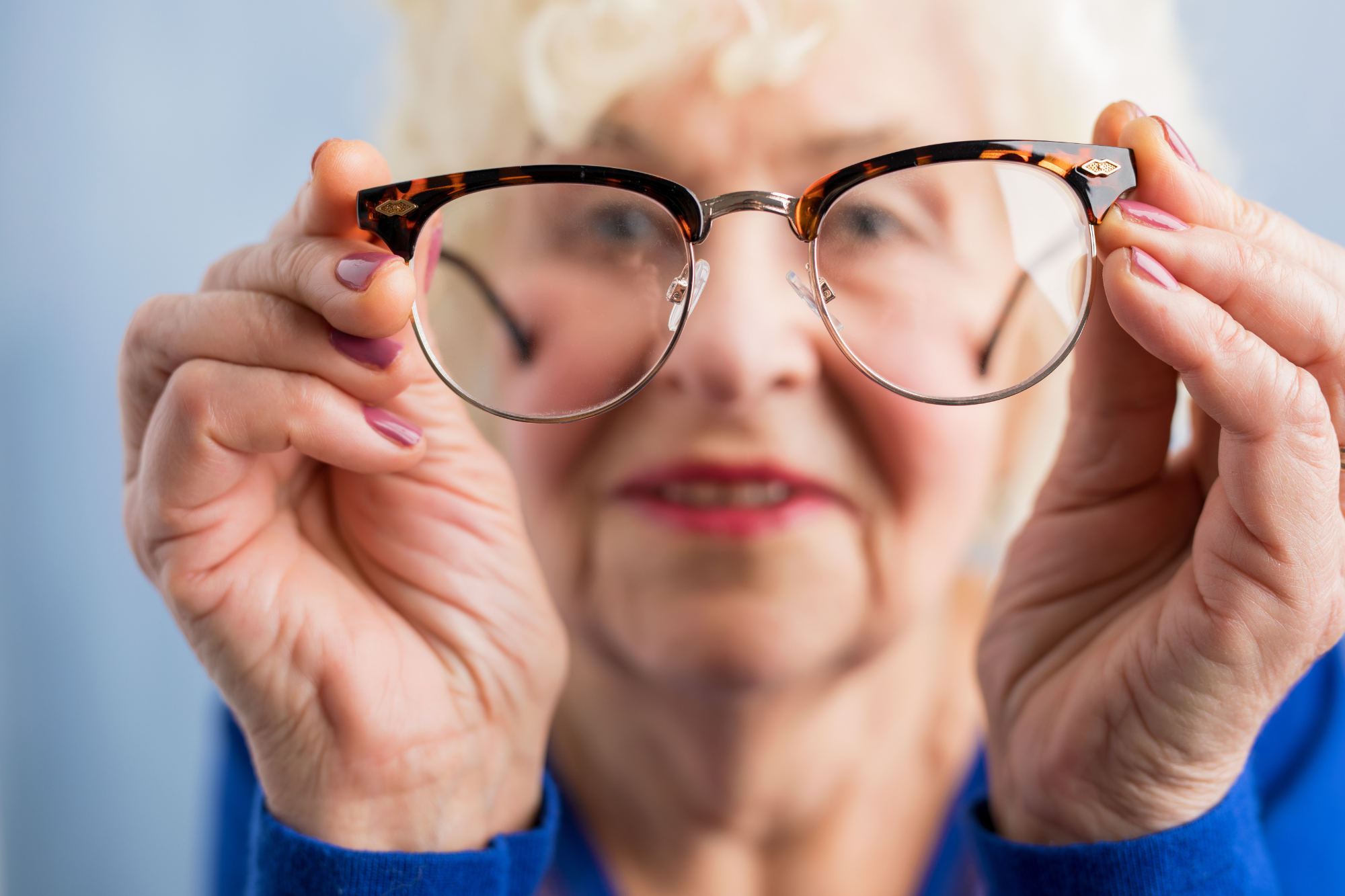 senior woman holding up a pair of eye glasses