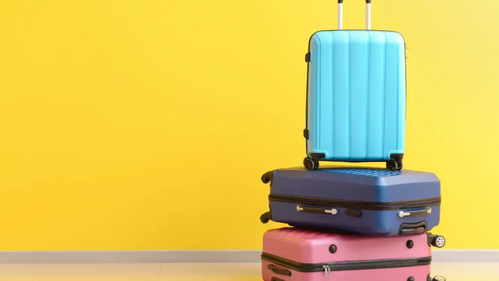 three colorful suitcases stacked on top of one another with a bright yellow background, it's probably moving day or time to travel