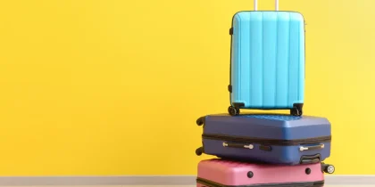 three colorful suitcases stacked on top of one another with a bright yellow background, it's probably moving day or time to travel