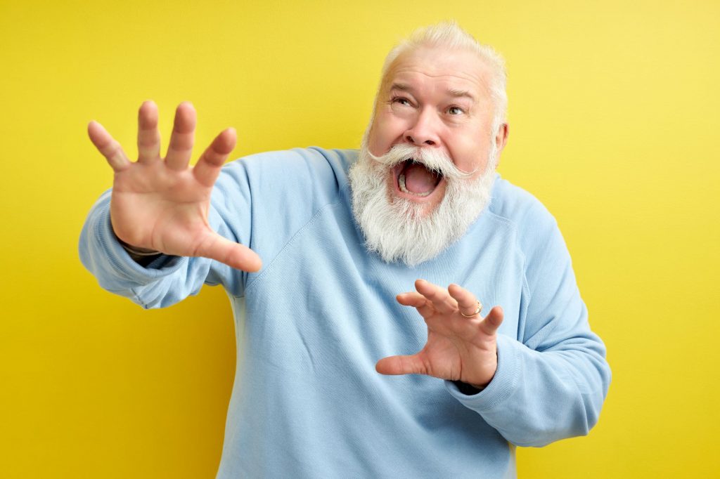 65 year old man with white beard, scared and raised hands in defense scared of parrot