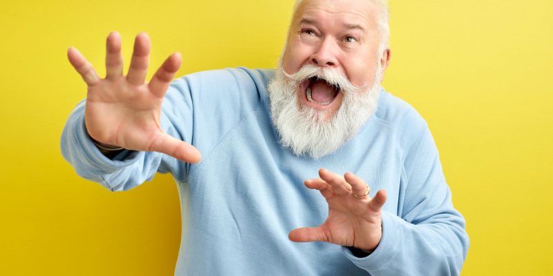 65 year old man with white beard, scared and raised hands in defense