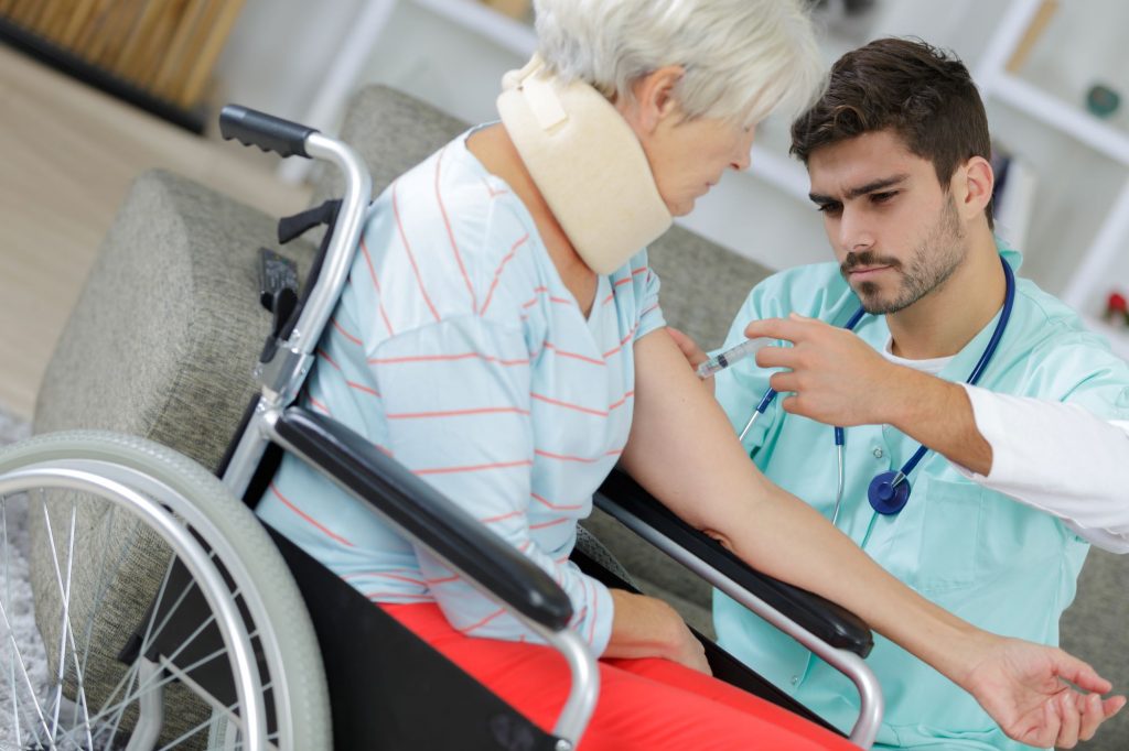 male nurse with a scruffy beard providing skilled nursing injection to a female resident in a wheelchair