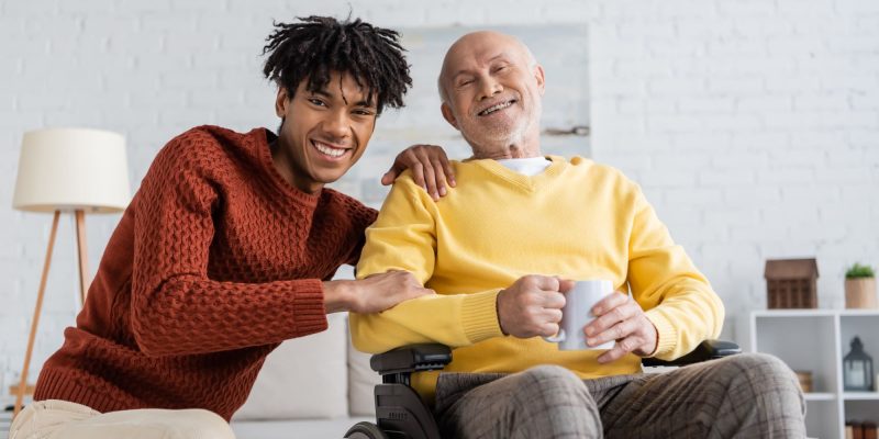 African American home caregiver and white senior in a wheelchair smiling