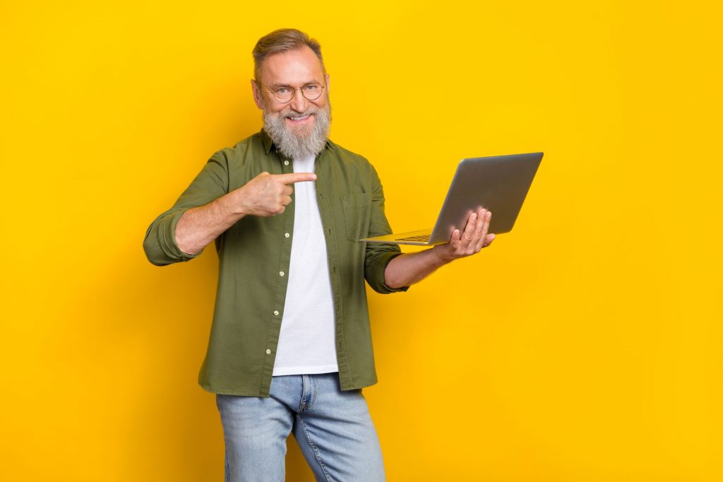 12 Fun Part-Time Job Ideas for Retirees cover photo of a retiree man with a beard holding a laptop and pointing