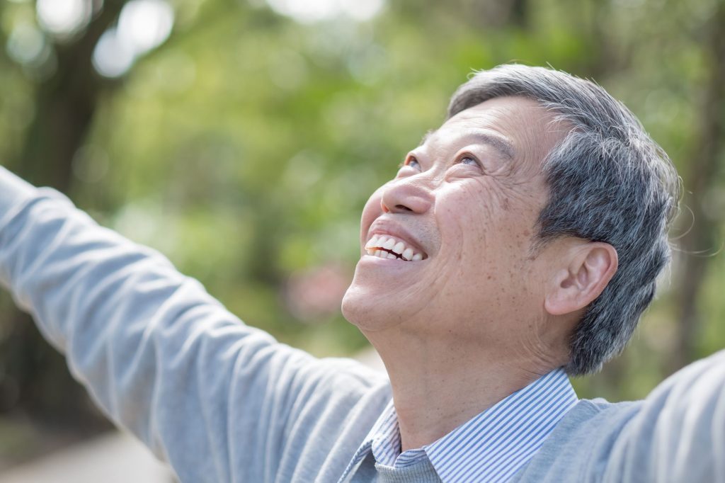 Asain Boomer man looking up at sky, smiling because he has let subtraction work for him