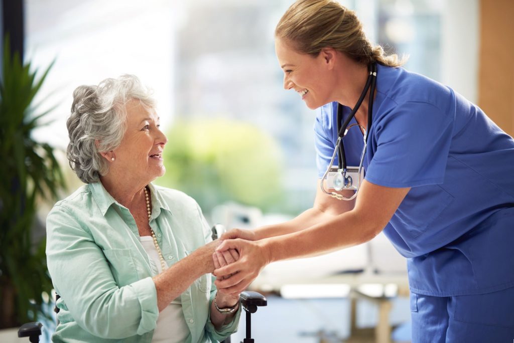 Senior woman sitting in a wheelchair in assisted living, talking with a smiling nurse