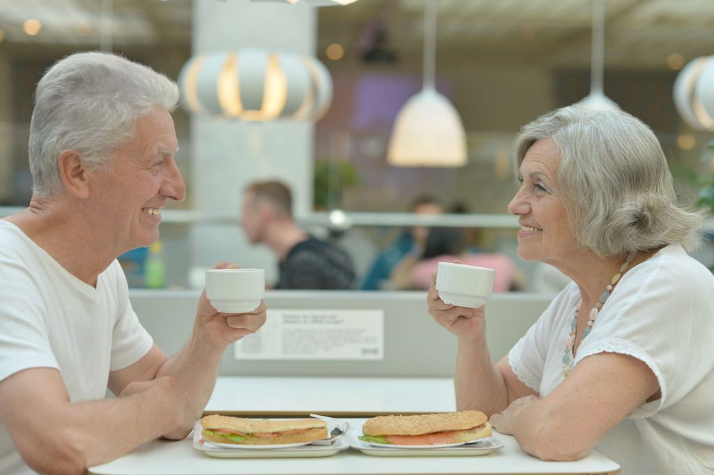 Senior couple enjoying coffee and sandwiches while eating out.