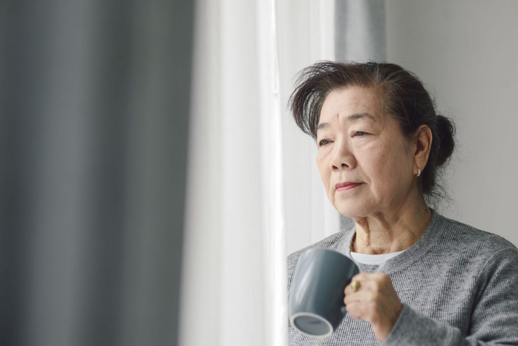 chronic loneliness concept art with lonely asiain senior woman looking out window and holding a coffee mug