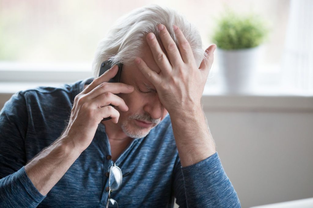upset senior man on phone with hand on head and eyes closed