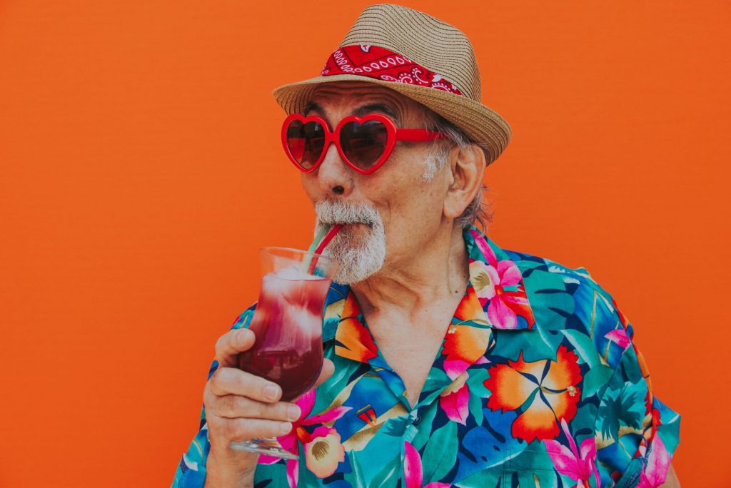 Older man with sunglasses and flowered shirt drinking a cocktail