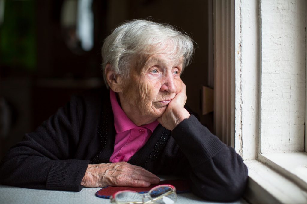 senior woman looking sad and lonely out of a window