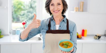 senior woman holding bowl of soup and giving thumbs up