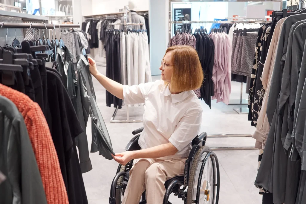Woman shopper in a wheelchair chooses clothes in the mall, adaptive clothing