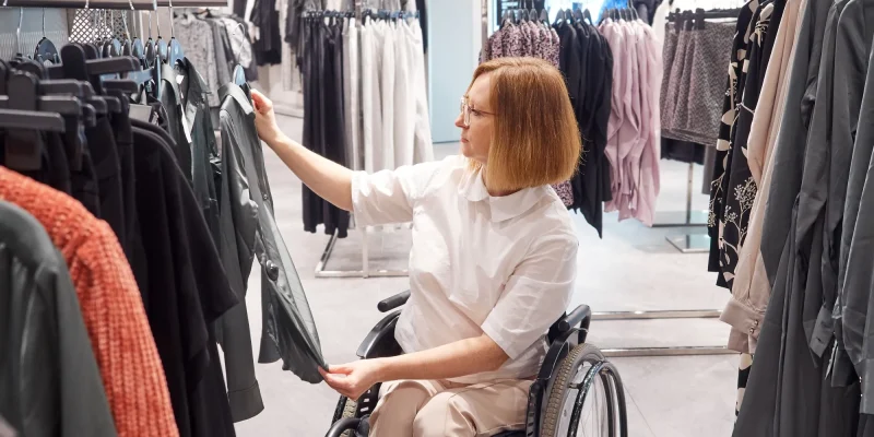 Woman shopper in a wheelchair chooses clothes in the mall, adaptive clothing
