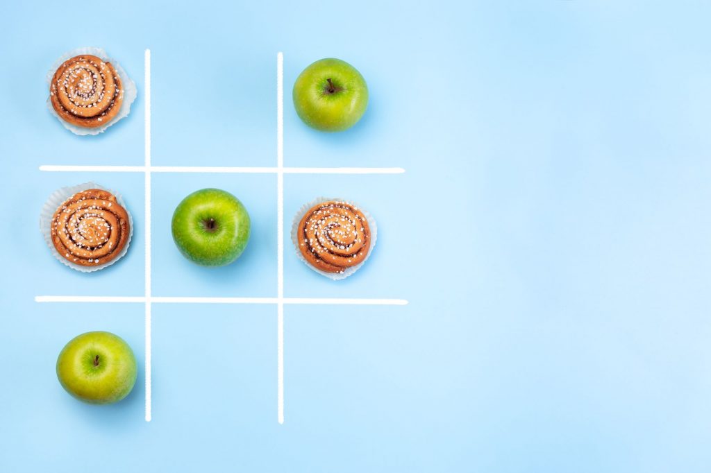 healthy choices vs unhealthy choices cocept with fruit and cinnamon roll tic tac toe