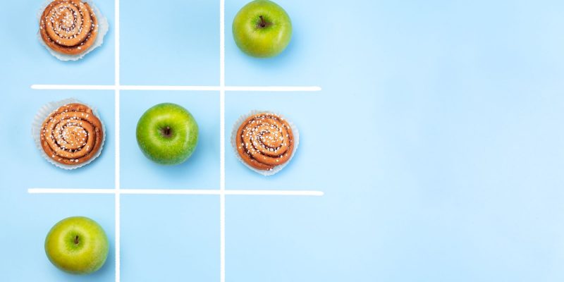healthy choices vs unhealthy choices cocept with fruit and cinnamon roll tic tac toe