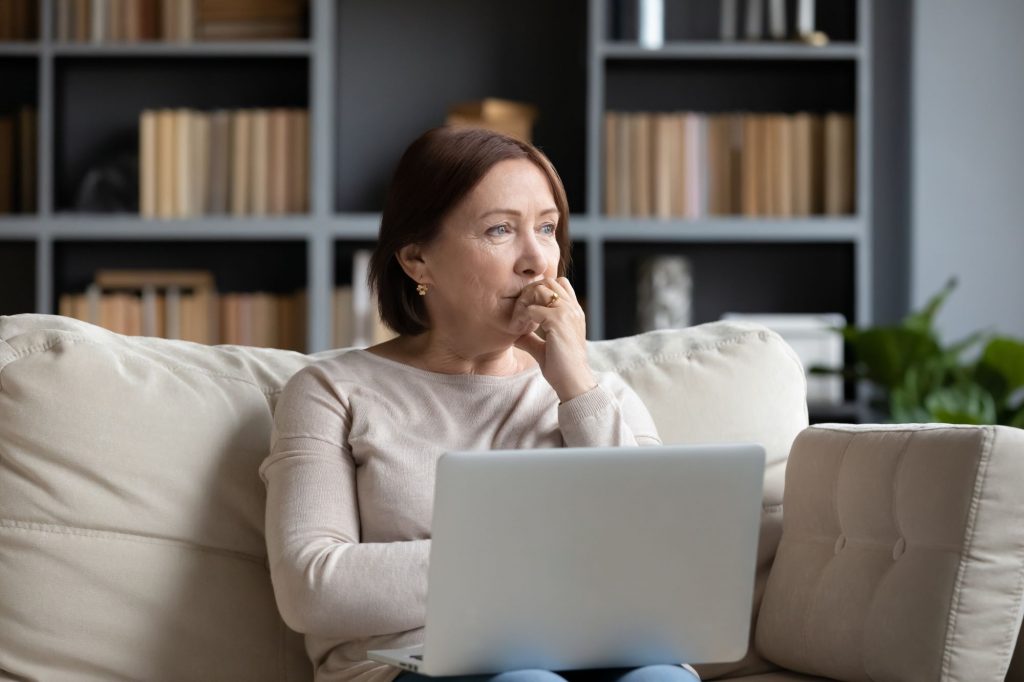 pensive senior woman using computer on the couch