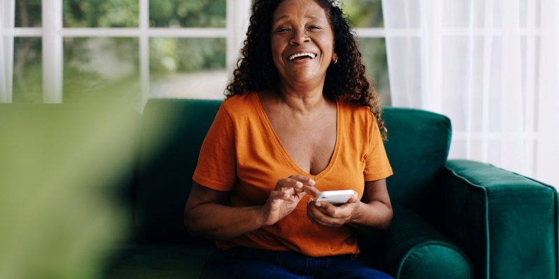 black woman retiree smiling and sitting on couch with phone
