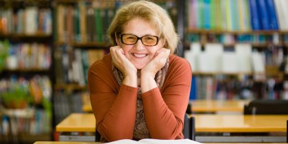 smiling senior woman sitting at a table in a library, maybe volunteering