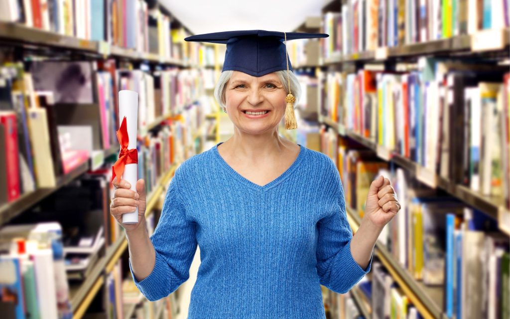 senior woman wearing a grad cap and holding a diploma in the middle of a library