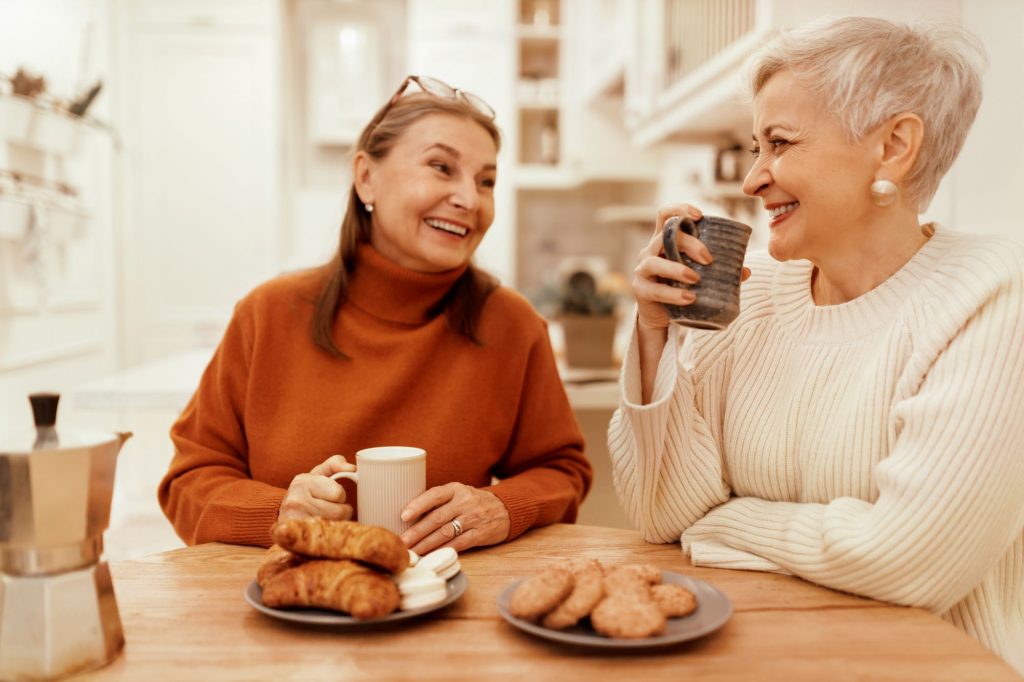 two senior women who live in a shared housing situation drinking coffee together at the kitchen table