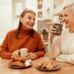 two senior women sitting at the kitchen table drinking cofee together
