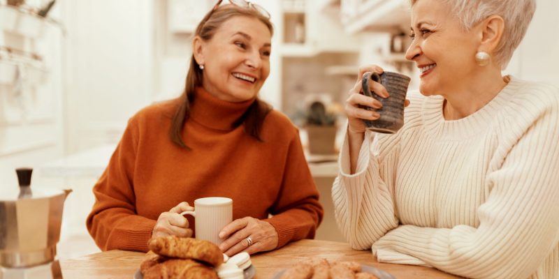 two senior women sitting at the kitchen table drinking cofee together