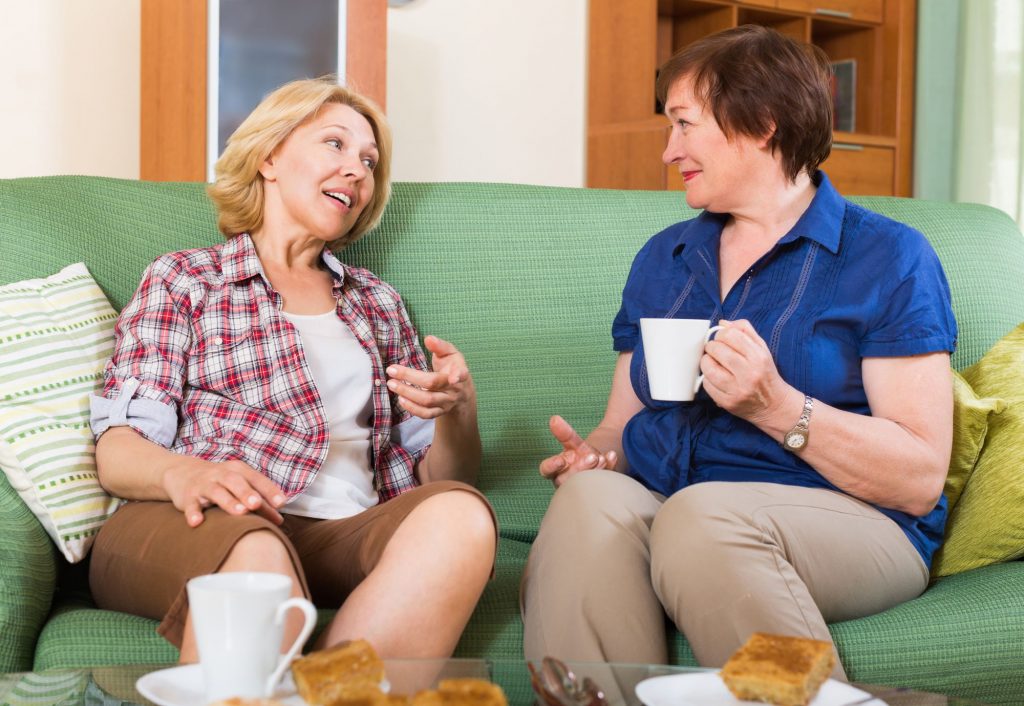 two older women friends talking on couch with coffee