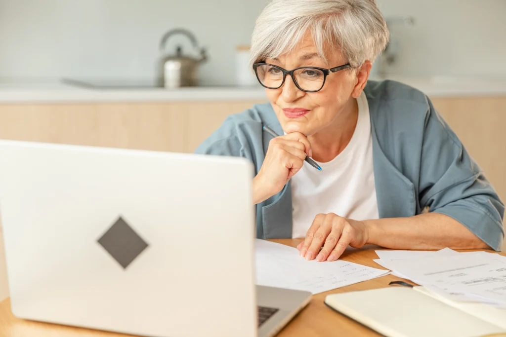 Online education courses webinar concept. Middle aged senior woman using laptop computer writing notes. Focused mature old woman enjoying studying online from home written records doing online work