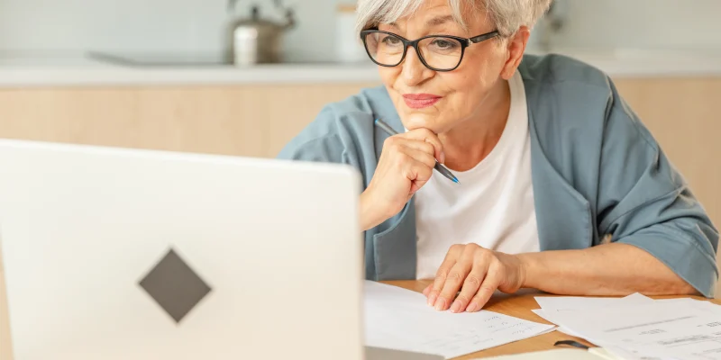 Online education courses webinar concept. Middle aged senior woman using laptop computer writing notes. Focused mature old woman enjoying studying online from home written records doing online work