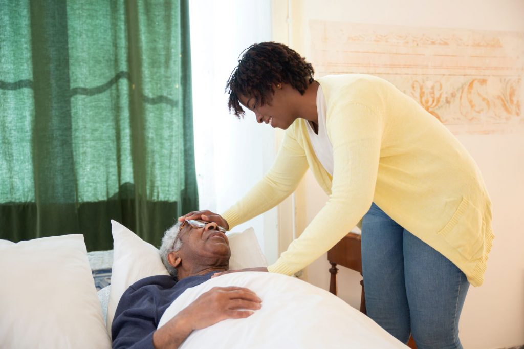 senior in bed receiving hospice care at home from a caregiver
