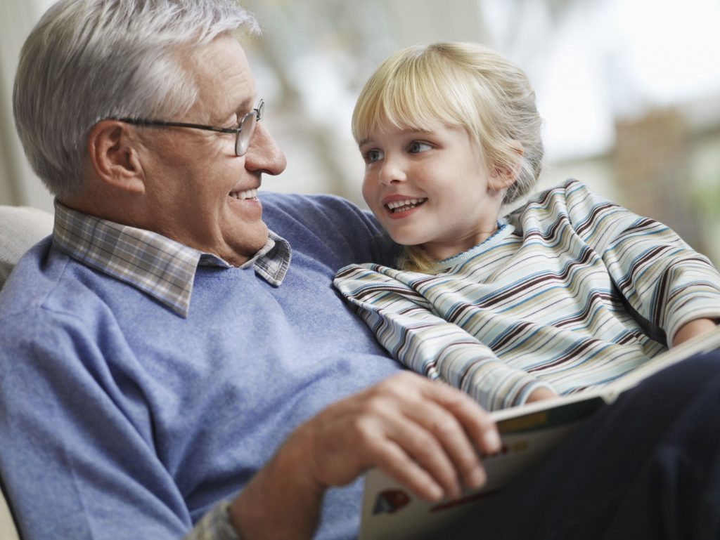 senior man sitting down with granddaughter, smiling