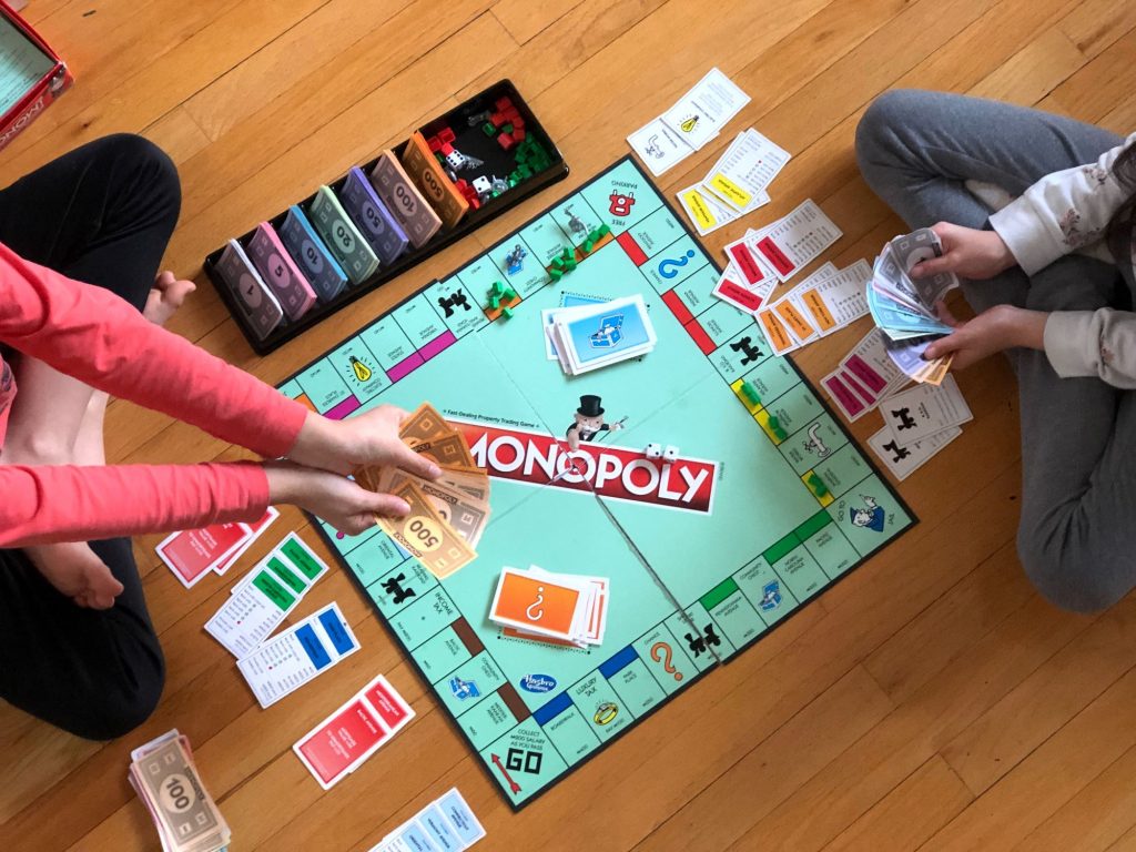 two children sitting on a wooden floor playing Monopoly