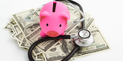 piggy bank sitting on pile of money with a stethescope