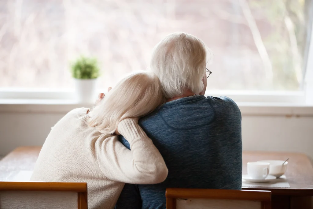 senior couple sitting in the kitchen looking out the window, view from back
