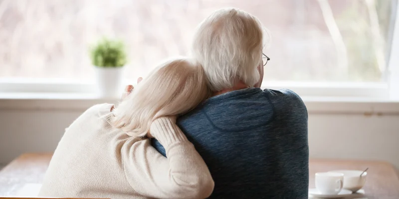 senior couple sitting in the kitchen looking out the window, view from back