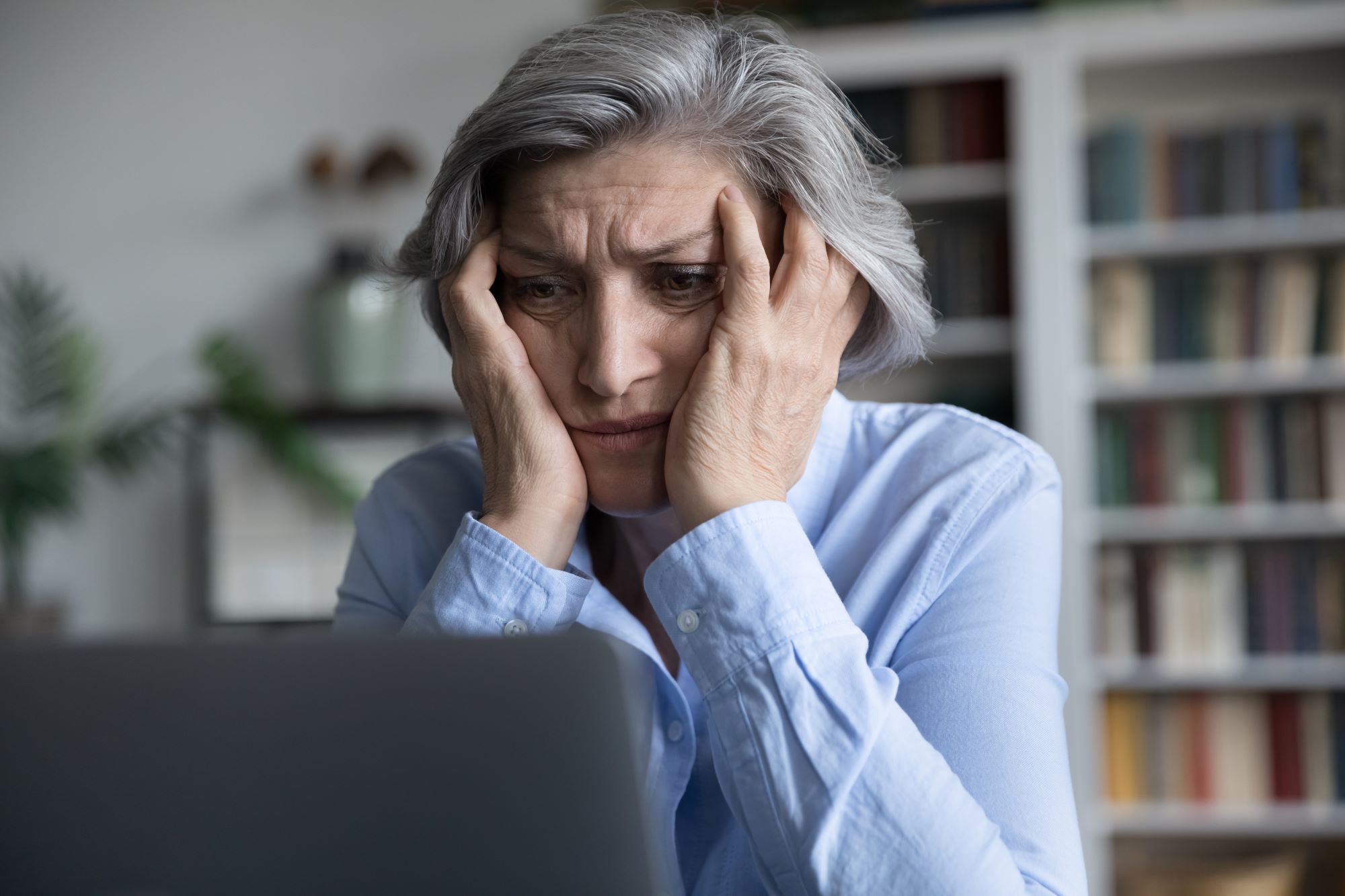 Senior woman with hands on face staring at a computer in frustration. 