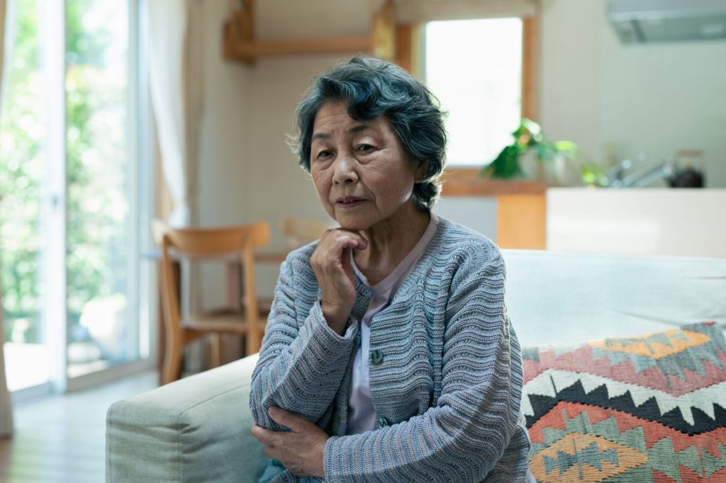 pensive asian lady sitting on her bed thinking