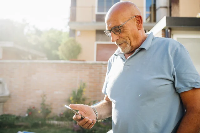 senior man standing outside puttering around on his phone