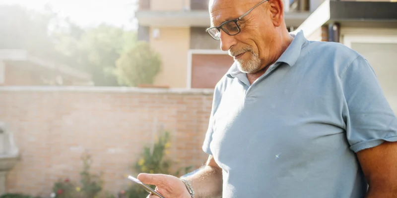 senior man standing outside puttering around on his phone