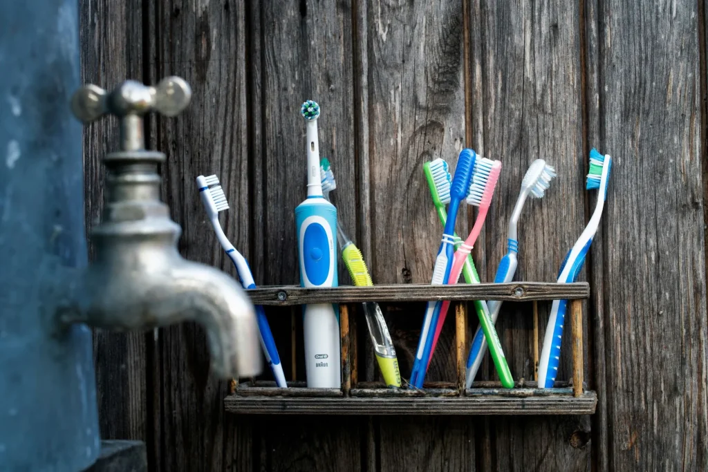 multiple toothbrushes stored together, wood background, faucet nearby