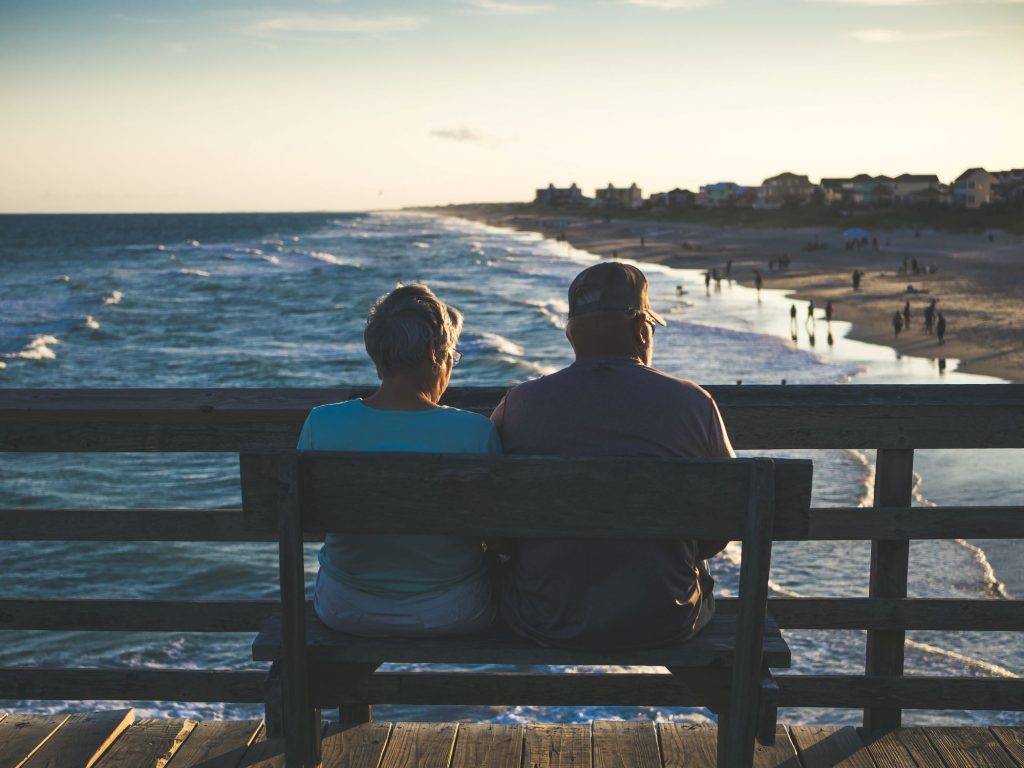 retirement couple sitting on a bench looking at waves