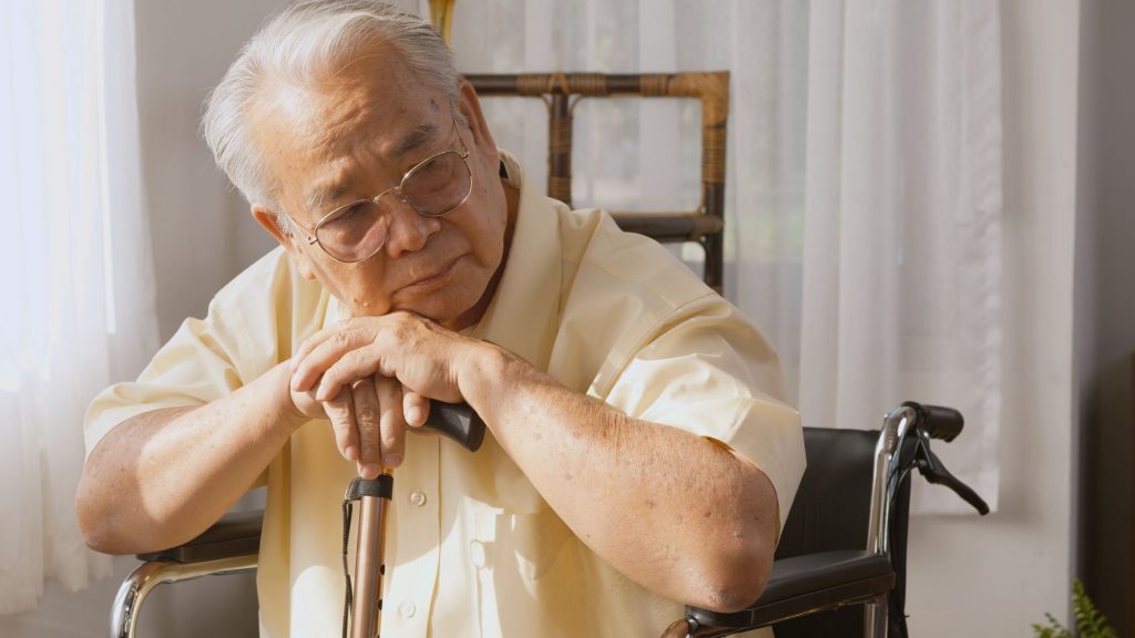 Elderly Asain man in a wheelchair holding cane