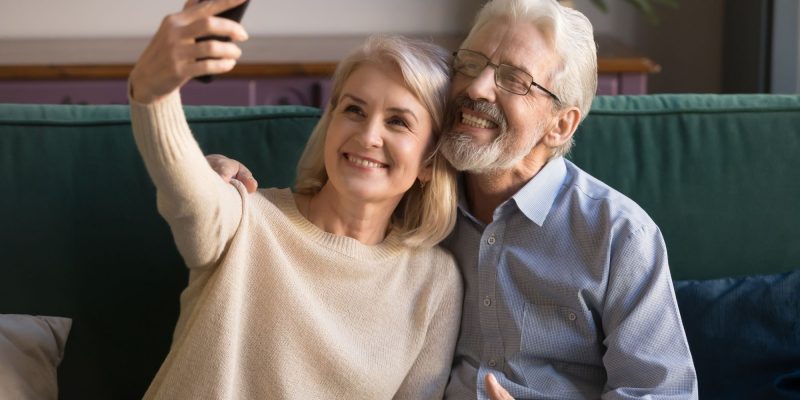 retired couple sitting on the couch smiling and taking a selfie