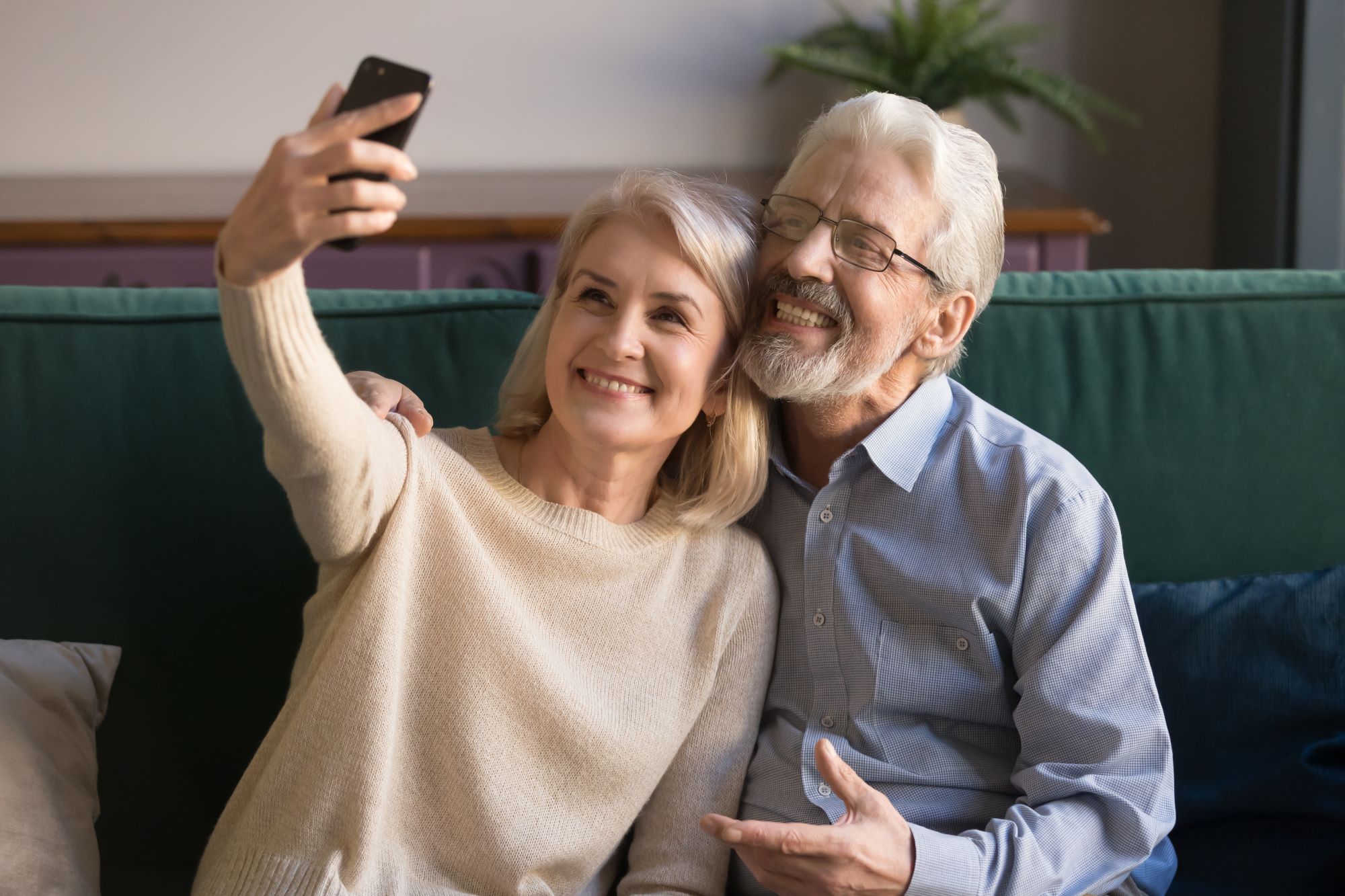 retired couple sitting on the couch smiling and taking a selfie